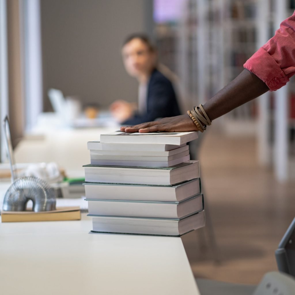 Close up of books and teaching aids taken by student on library bookshelves in pile stacked on table for study or prepare for exams. Power in knowledge. Effective obtaining second higher education.